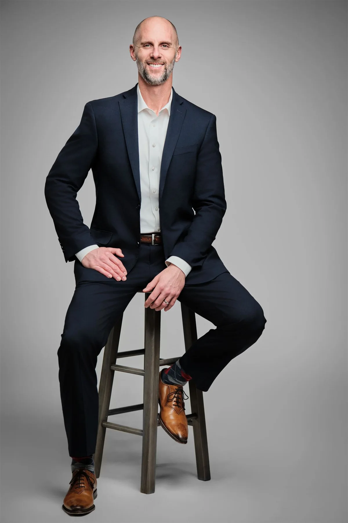 Man in a dark suit seated on a stool, by Henry David Photography